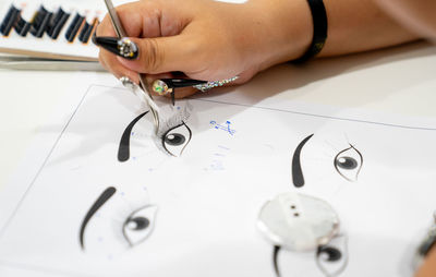 Cropped hand of woman adjusting eyelash on paper at store