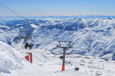 Chairlift with skiers on the background of snowy peaks and blue sky