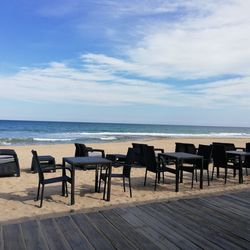 Empty chairs and table on beach against sky
