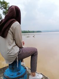 Side view of woman sitting on bollard against lake