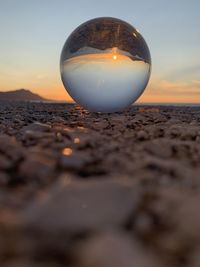 Close-up of crystal ball on beach against sky during sunset