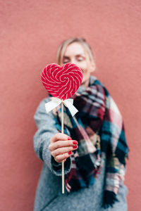 Woman holding heart shaped lollipop against wall