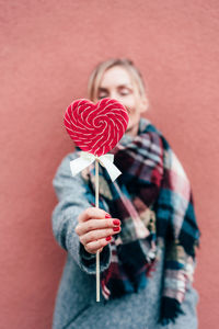 Portrait of woman holding ice cream standing against red wall