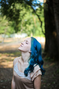 Young woman looking away while standing on tree in forest