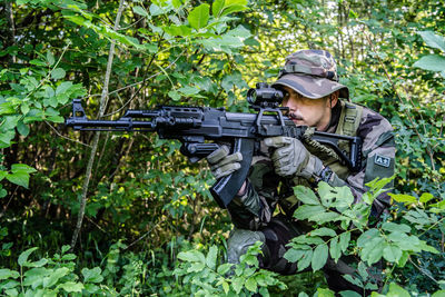 Soldier holding gun while hiding amidst plants