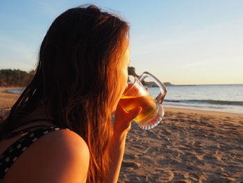 Side view of young woman drinking alcohol at beach during sunset