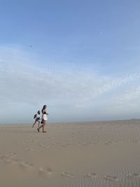 Two women on sand against sky