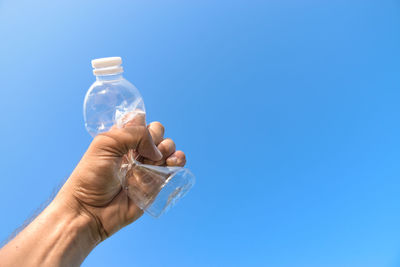 Cropped hand of man holding crushed bottle against sky