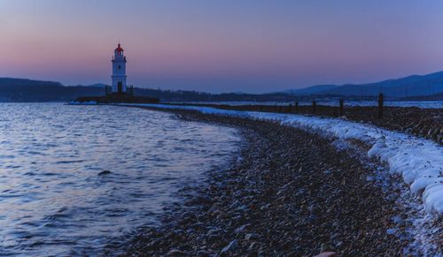 Lighthouse by sea against sky during sunset