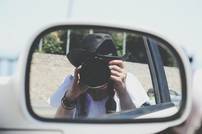 Reflection of woman photographing using camera on car side-view mirror