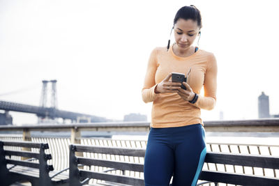 Sporty woman listening music through smart phone with williamsburg bridge in background