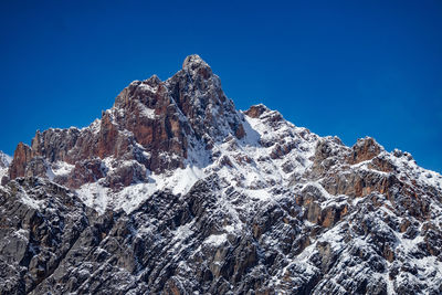 Low angle view of snowcapped mountains against clear blue sky