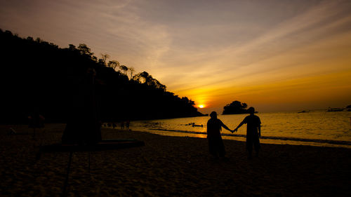 Silhouette people on beach against sky during sunset