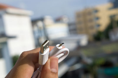 Close-up of hand holding usb cable against buildings