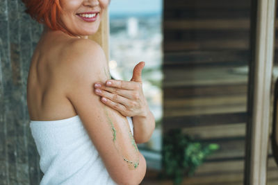 Young woman in white towel does body massage with organic natural scrab in sauna, treat yourself