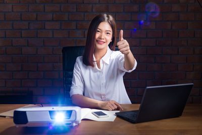 Portrait of smiling young woman using phone on table