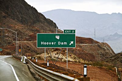 Directional road sign on roadside against mountains