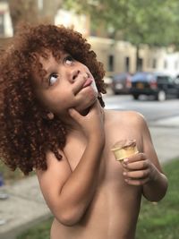 Thoughtful shirtless boy having ice cream cone while standing outdoors
