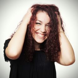 Smiling happy woman with hands in hair against wall