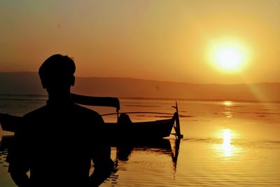 Silhouette man in sea against sky during sunset