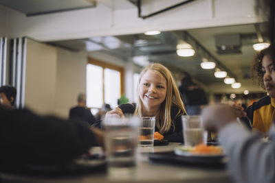 Smiling girl enjoying food with friends during lunch break at school