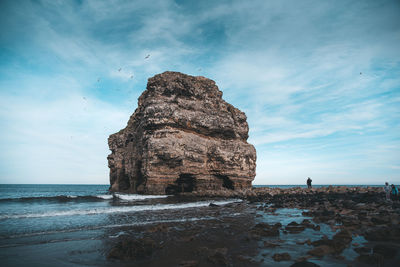 Rock formation on beach against sky