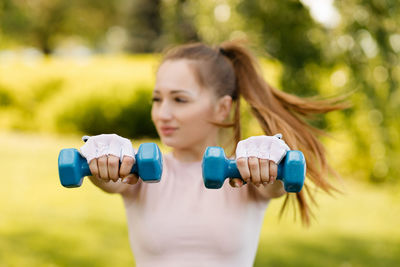 Sports girl doing exercise with dumbbells in the park