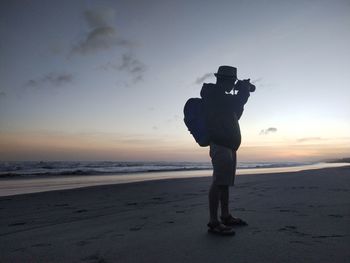 Man photographing while sanding on beach against sky