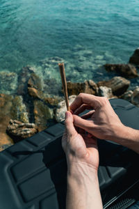 Cropped hand holding marijuana joint against sea