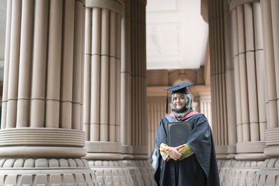 Portrait of smiling young woman wearing graduation gown at university