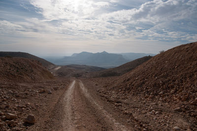 Dirt road leading towards mountains against sky