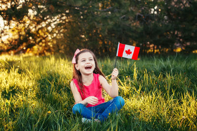Happy girl with canadian flag sitting on field