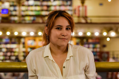 Portrait of smiling young woman standing against illuminated wall