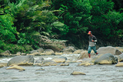 Side view of man standing on rock against trees