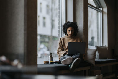 Businesswoman working on laptop by window in creative office