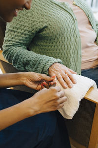 Midsection of senior woman getting her nails in shape from young female caretaker at nursing home