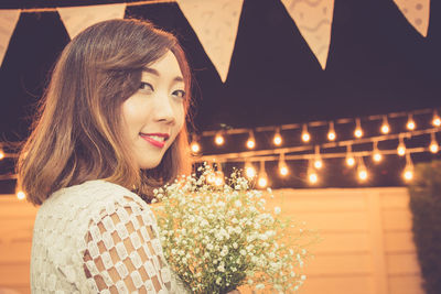 Portrait of woman with bouquet against illuminated decoration at night