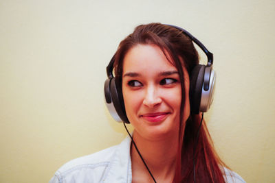 Close-up of woman looking away while wearing headphones against wall