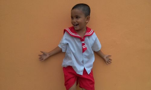 Portrait of smiling boy standing against orange wall