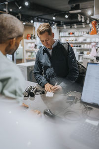 Mature man signing bill at checkout counter in appliances store