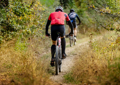 Back man on mountain bike riding on mountain trail with dry grass