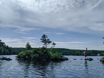 Man on rock in river against sky