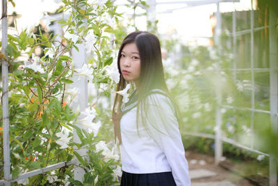 Side view of young woman standing against plants