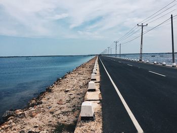 Empty road and power lines next to sea