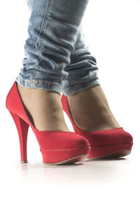 Low section of woman wearing red shoes standing against white background