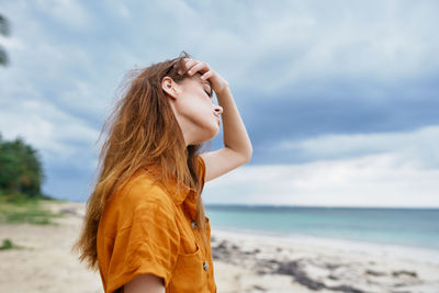 Young woman standing at beach against sky