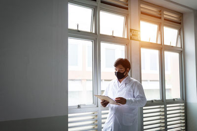 Woman looking through smart phone while standing on window