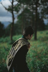 Side view of young man walking in forest against trees