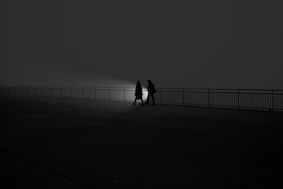 Silhouette people walking on bridge against clear sky