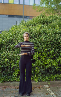 Full length portrait of woman gesturing while standing against plants